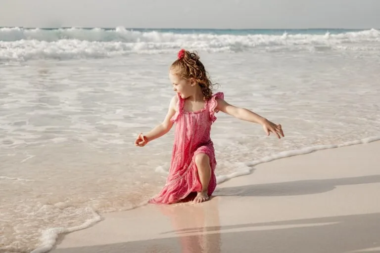 Little girl in a pink dress playing at the water’s edge during a family photo session near Hilton Cancun Mar Caribe, by Pro Art Photographers